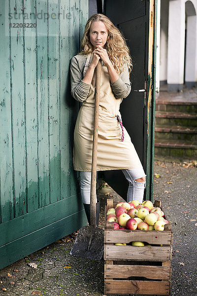 Porträt einer selbstbewussten Frau  die an einer Kiste mit Äpfeln steht.