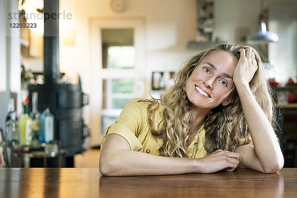 Porträt einer lächelnden  blonden Frau  die sich auf den Tisch lehnt.