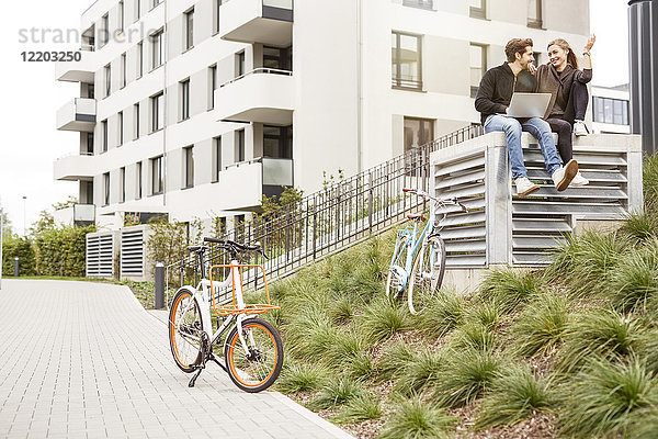 Glückliches Paar mit Fahrrädern und Laptop in urbaner Umgebung