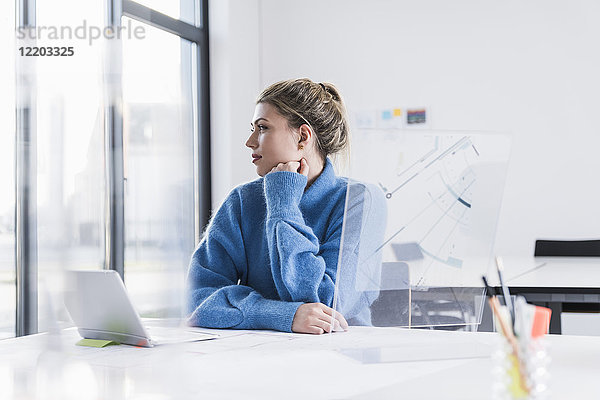 Junge Frau mit Laptop und transparentem Design am Schreibtisch im Bürodenken