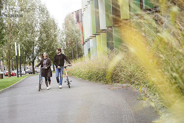 Lächelndes Paar  das mit Fahrrädern auf einer Straße spazieren geht