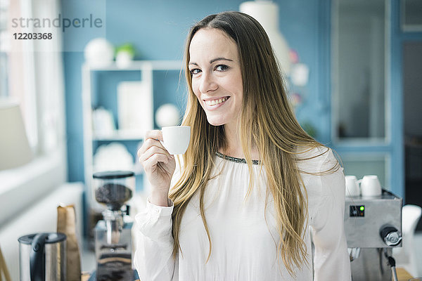 Porträt einer glücklichen Geschäftsfrau  die in der Küche eines Loftes Espresso trinkt.
