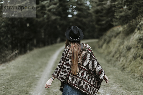 Rückansicht der modischen jungen Frau mit Hut und Poncho in der Natur