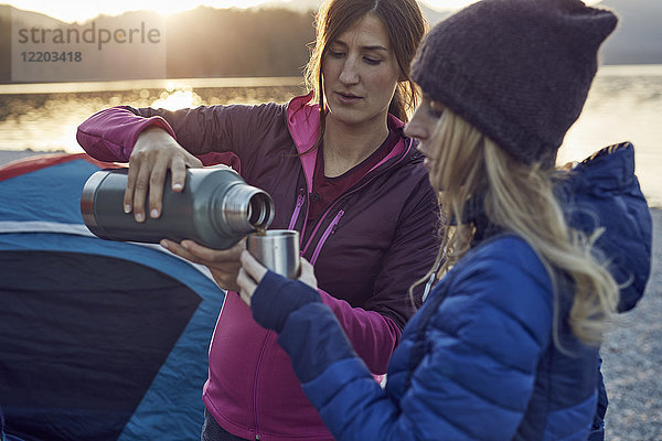 Zwei Frauen mit heißem Getränk beim Camping am Seeufer