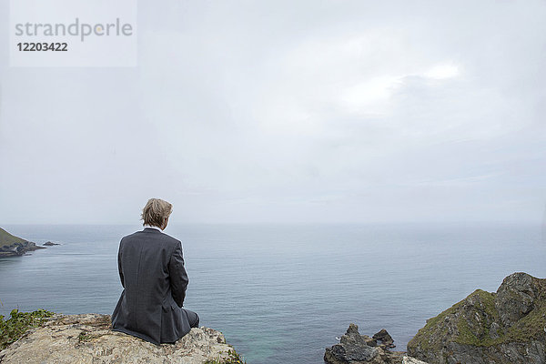 UK  Cornwall  Gwithian  Geschäftsmann an der Küste sitzend mit Blick auf die Aussicht