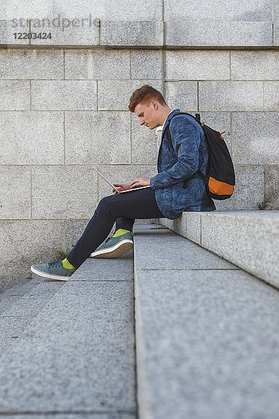 Rothaariger junger Mann auf der Treppe sitzend mit Laptop