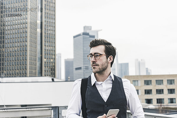 Deutschland  Frankfurt  junger Geschäftsmann mit Handy in der Stadt schaut sich um