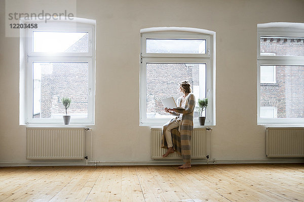 Reife Frau im leeren Raum mit Laptop am Fenster