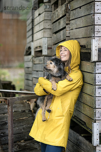 Lächelnde Frau auf einem Bauernhof stehend an Holzkisten mit Hund