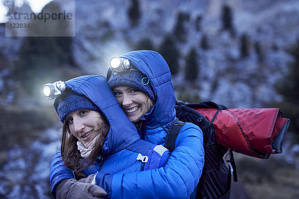 Zwei glückliche junge Frauen mit Scheinwerfern  die sich in den Bergen umarmen.