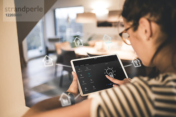 Frau sitzt zu Hause und benutzt ein digitales Tablett  um sein intelligentes Zuhause fernzusteuern.