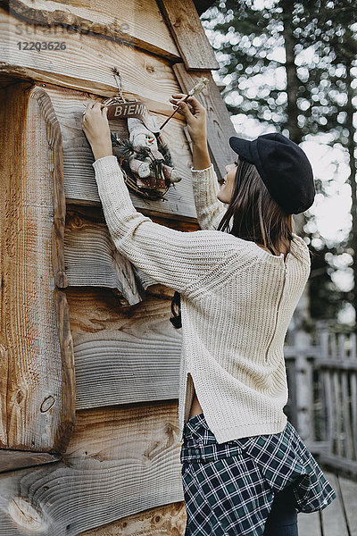 Junge Frau schmückt Holzhaus mit Weihnachtsdekoration