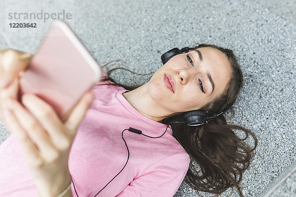 Entspannte junge Frau im Liegen mit Handy und Kopfhörer