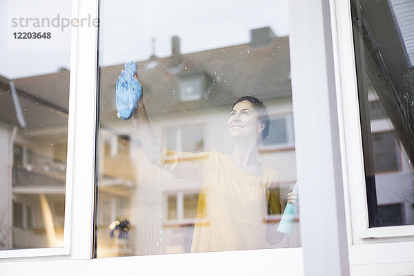 Lächelnde Frau zu Hause beim Fensterputzen