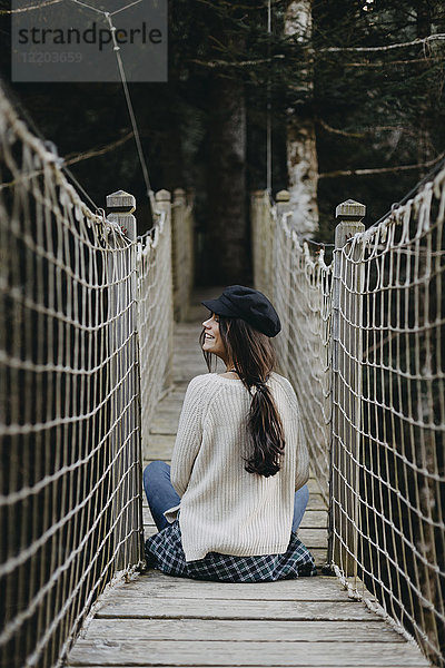 Lächelnde junge Frau auf einer Hängebrücke sitzend
