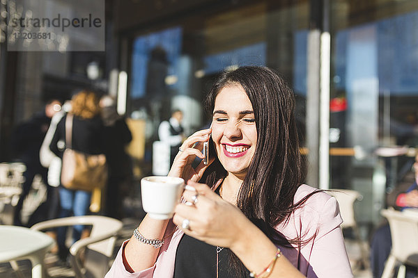 Lachende junge Geschäftsfrau am Handy in einem Outdoor-Café