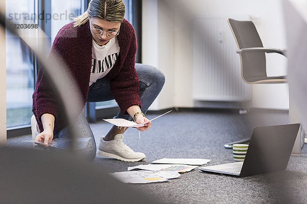 Junge Frau mit Laptop und Dokumenten  die auf dem Boden im Büro arbeiten
