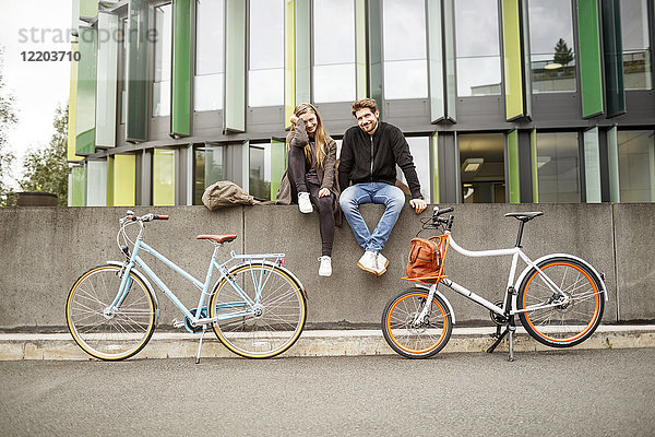 Glückliches Paar mit Fahrrädern an der Wand sitzend