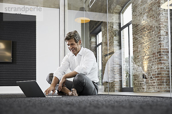 Barfuß Geschäftsmann mit Laptop auf dem Boden im modernen Büro