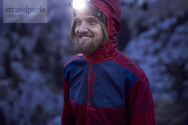 Porträt eines lächelnden Mannes mit Stirnlampe bei Dämmerung in den Bergen