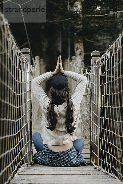 Junge Frau in Yoga-Pose auf einer Hängebrücke sitzend