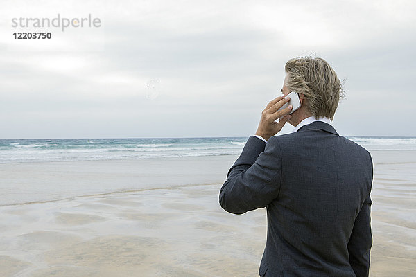 UK  Cornwall  Hayle  Geschäftsmann am Strand im Gespräch mit dem Handy