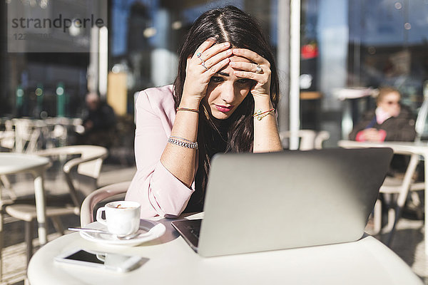 Frustrierte junge Geschäftsfrau mit Laptop in einem Outdoor-Café
