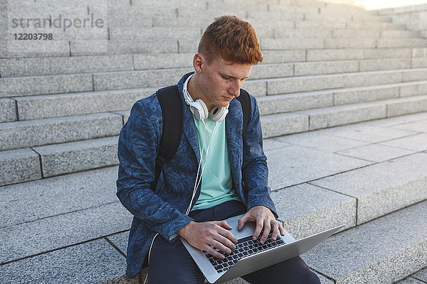 Rothaariger junger Mann auf der Treppe sitzend mit Laptop