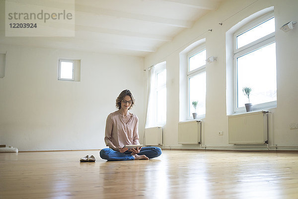 Reife Frau sitzend auf dem Boden im leeren Raum mit Tablette