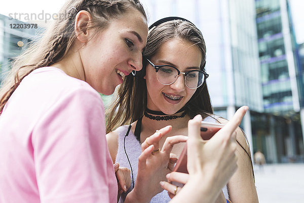 Zwei glückliche Teenager-Mädchen teilen sich ihr Handy in der Stadt.
