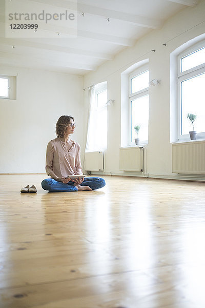 Reife Frau auf dem Boden sitzend in leerem Raum mit Tablette
