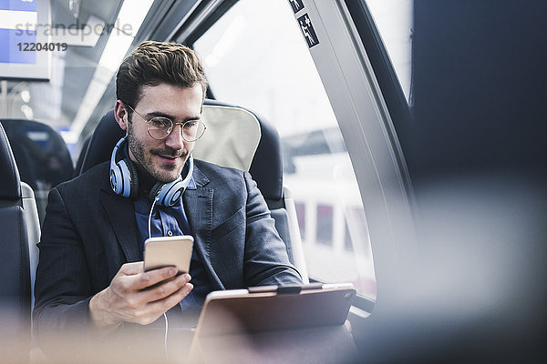 Geschäftsmann im Zug mit Handy  Kopfhörer und Tablett