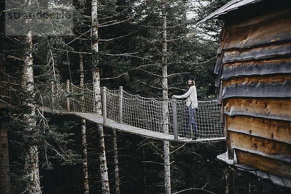 Junge Frau auf einer Hängebrücke am Baumhaus im Wald