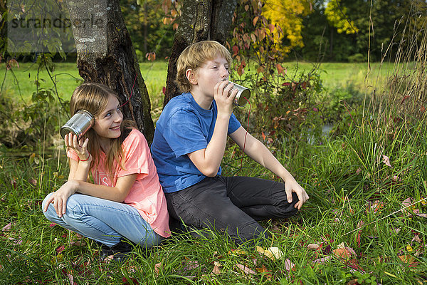 Junge und Mädchen auf einer Wiese haben Spaß mit Blechdosentelefonen