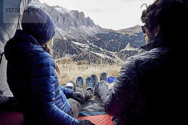 Paar sitzt im Zelt in den Bergen und schaut auf die Aussicht.