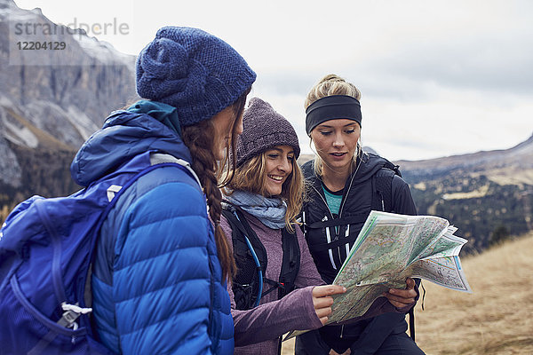 Drei junge Frauen beim Wandern in den Bergen mit Blick auf die Karte