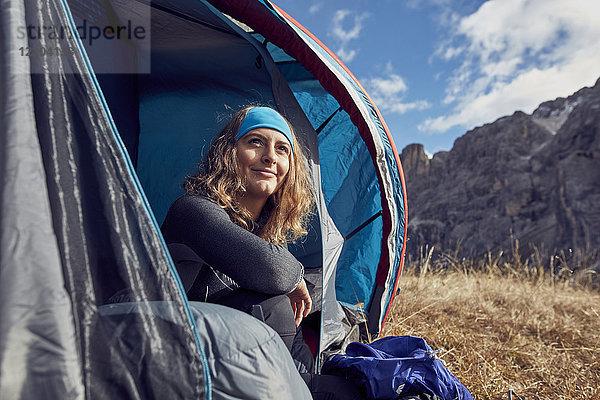 Lächelnde junge Frau im Zelt in den Bergen sitzend