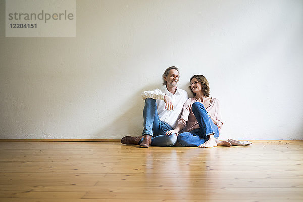 Lächelndes reifes Paar sitzt auf dem Boden in einem leeren Raum.