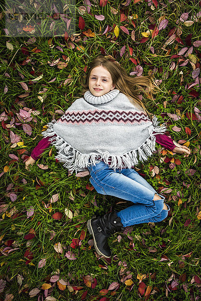 Porträt eines lächelnden Mädchens mit Poncho auf herbstlicher Wiese liegend