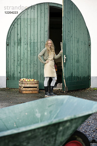 Lächelnde Frau auf einem Bauernhof stehend an einer Kiste mit Äpfeln