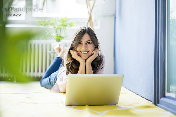 Porträt einer lächelnden Frau auf dem Boden liegend mit Laptop