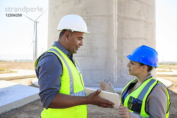 Zwei Ingenieure mit Tablette diskutieren auf einem Windpark