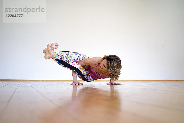 Reife Frau  die Yoga auf dem Boden in einem leeren Raum praktiziert.