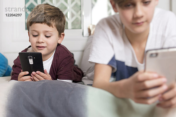 Zwei Jungen  die zu Hause auf dem Bett liegen und Handys benutzen.
