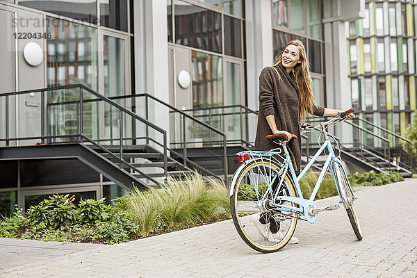 Lächelnde Frau mit Fahrrad vor einem Gebäude stehend