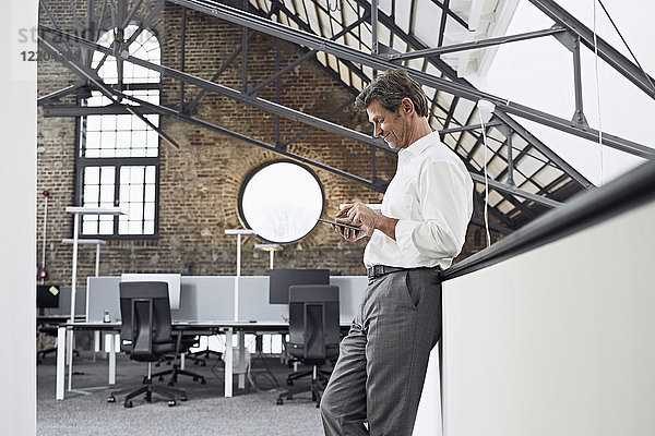 Ausgereifter Geschäftsmann mit Smartphone im modernen Büro