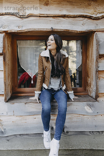 Glückliche junge Frau sitzt auf der Fensterbank eines Holzhauses