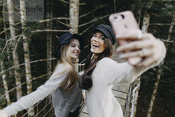 Zwei glückliche junge Frauen auf einer Hängebrücke  die einen Selfie nehmen.