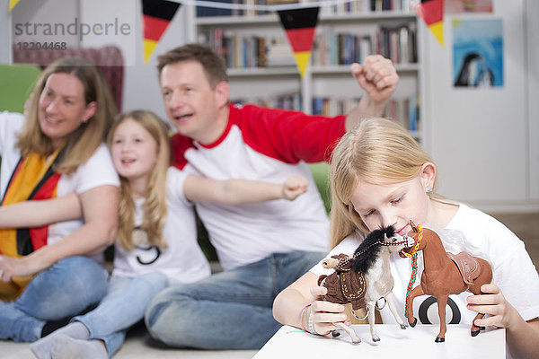 Familie schaut Fußballweltmeisterschaft im Fernsehen  während das kleine Mädchen mit Spielzeug spielt.