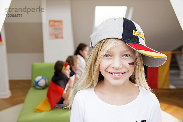 Porträt eines Mädchens mit deutscher Gesichtsbemalung und Mütze mit Freunden im Hintergrund